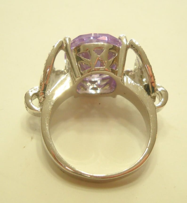 May include: A silver ring with a large, clear, purple gemstone set in a decorative, open-work setting.