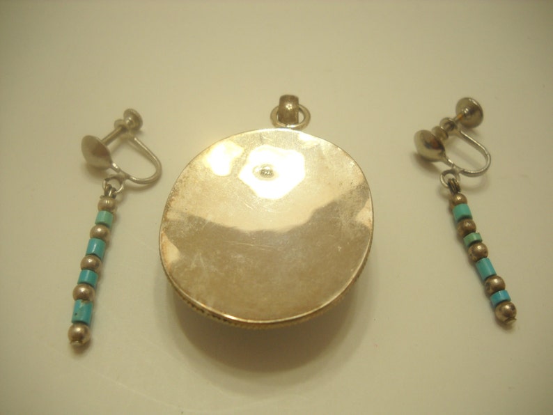 Op de afbeelding: Een zilveren hanger met een turquoise steen en een bijpassend paar oorclips met turquoise kralen.
