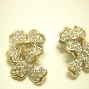 May include: A pair of gold tone clip-on earrings with a flower design. The earrings are adorned with clear rhinestones.