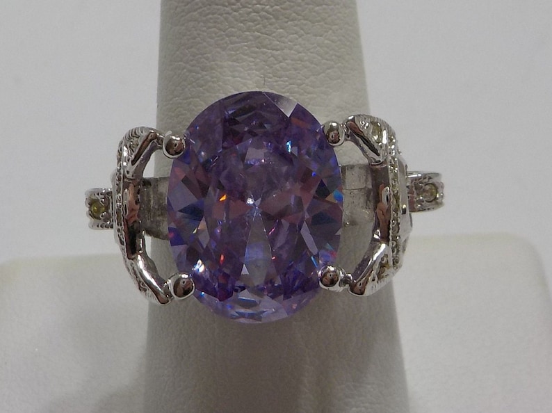 May include: A silver ring with a large, oval-shaped, purple gemstone surrounded by smaller clear gemstones.