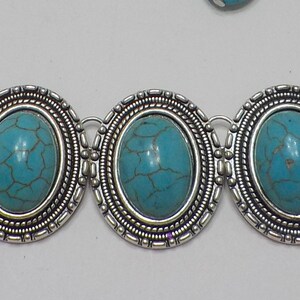 May include: A silver chain bracelet with five oval turquoise stones set in silver bezels. The stones have a marbled pattern.