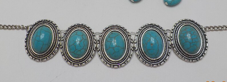 May include: A silver chain bracelet with five oval turquoise stones set in silver bezels. The stones have a marbled pattern.