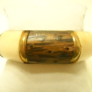 May include: A wooden bangle bracelet with a gold trim and ivory colored ends.