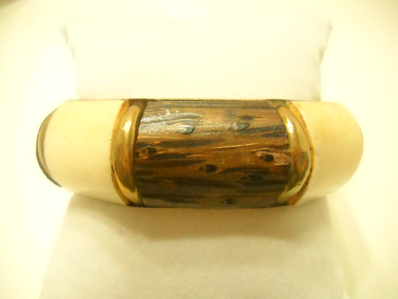 May include: A wooden bangle bracelet with a gold trim and ivory colored ends.