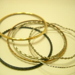 May include: A set of six gold, silver, and black bangles. The bangles are stacked on top of each other and are arranged in a circle.
