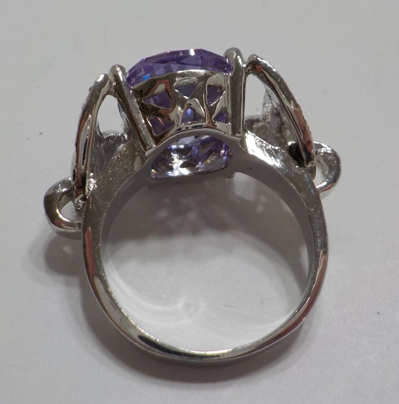 May include: A silver ring with a large, clear, purple gemstone set in a decorative, open-work setting.
