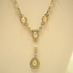 May include: A silver necklace with a teardrop pendant and oval-shaped iridescent stones. The necklace has a delicate chain and intricate detailing.