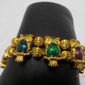 May include: A gold-tone bracelet featuring a series of owl-shaped charms with colorful enamel detailing in shades of blue, green, and purple, interspersed with ribbed gold-tone spherical beads. The date 07.10.2026 is printed in the bottom right corner.