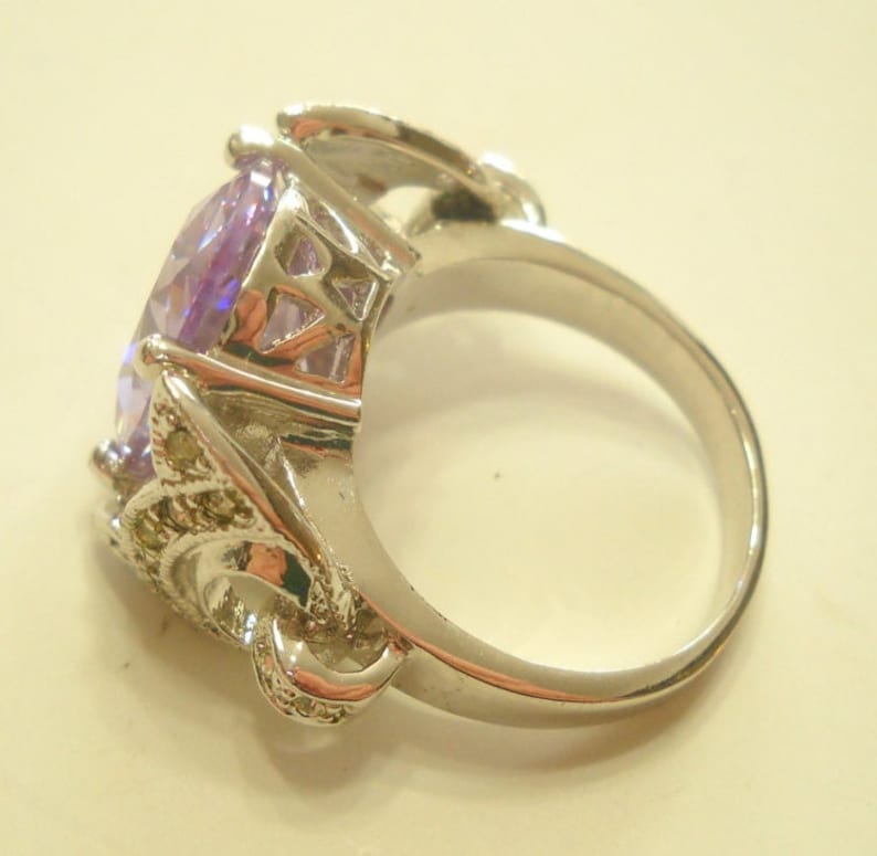 May include: A silver ring with a large, oval-shaped, purple gemstone set in a decorative, ornate setting.