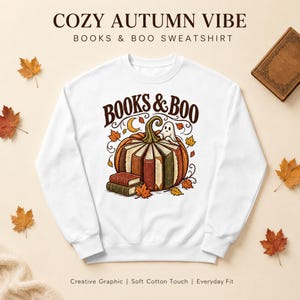 Puede incluir: Una sudadera blanca de cuello redondo con un gráfico de una calabaza hecha de libros con un pequeño fantasma encima. El texto dice BOOKS & BOO. El diseño incluye hojas de otoño y una luna creciente sobre un fondo de color claro.