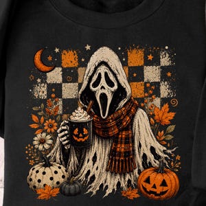 May include: A black sweatshirt featuring a graphic of a ghost wearing a plaid scarf and holding a mug with a jack-o'-lantern face. The design includes orange and white checkered patterns, autumn leaves, daisies, a crescent moon, and pumpkins.