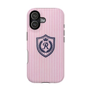 Peut inclure: Une coque de téléphone à rayures verticales roses et blanches avec un écusson bleu foncé au centre. L'écusson affiche une couronne au-dessus d'une couronne de laurier entourant la lettre R. La coque présente un module photo noir en haut à gauche.