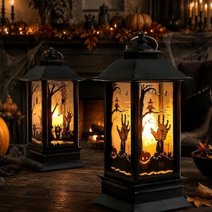 May include: Two black rectangular lanterns with a top handle, featuring translucent panels decorated with silhouettes of trees, pumpkins, owls, and reaching hands. The lanterns emit a warm, glowing light from within, creating a festive atmosphere.
