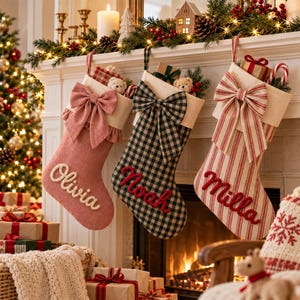 Könnte beinhalten: Drei Weihnachtsstrümpfe hängen in einer Reihe. Der erste ist einfarbig rosa mit einer großen Schleife und dem Namen Olivia. Der zweite ist schwarz-weiß kariert mit einer Schleife und dem Namen Noah. Der dritte ist rot-weiß gestreift mit dem Namen Milla.