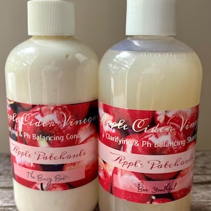 May include: Two clear plastic bottles with white pump tops and labels. The labels are red, white, and pink with the text "Apple Cider Vinegar" and "Apple Patchouli". One bottle says "Clarifying & Ph Balancing Shampoo" and the other says "Moisturizing & Ph Balancing Conditioner".