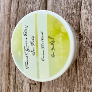 May include: A white jar with a yellow and green striped label. The label reads "French Green Clay & Sea Kelp Cream Face Wash Be Youtiful! 4-29-2009"