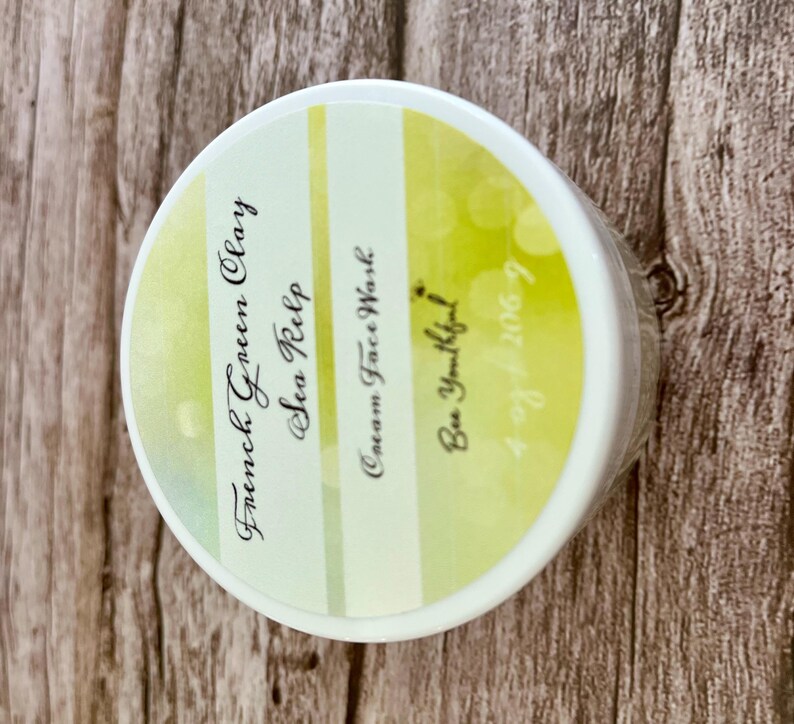 May include: A white jar with a yellow and green striped label. The label reads "French Green Clay & Sea Kelp Cream Face Wash Be Youtiful! 4-29-2009"