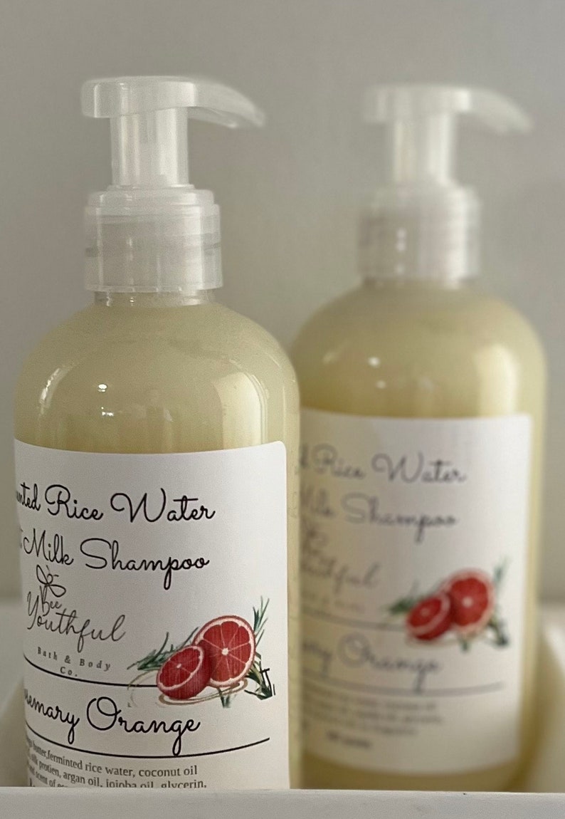 Puede incluir: Dos botellas de champ&uacute; transparentes con etiquetas blancas. Las etiquetas dicen "Fermented Rice Water & Milk Shampoo" y "Rosemary Orange". Cada etiqueta presenta un gr&aacute;fico de una naranja en rodajas y ramitas de romero. Las botellas tienen dispensadores de bomba blancos.