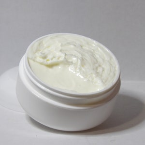 Könnte beinhalten: Ein weißer Plastikbehälter mit einem weißen Deckel, der teilweise mit einer weißen cremigen Substanz gefüllt ist. Der Deckel ist abgenommen und die Creme überläuft.