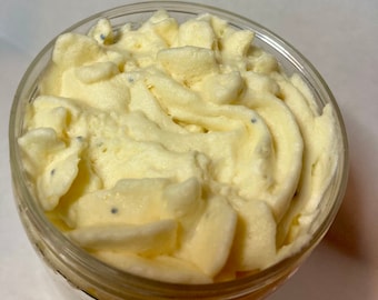 May include: A clear glass jar filled with a white whipped body butter. The butter has a swirl pattern and is topped with blue flecks.