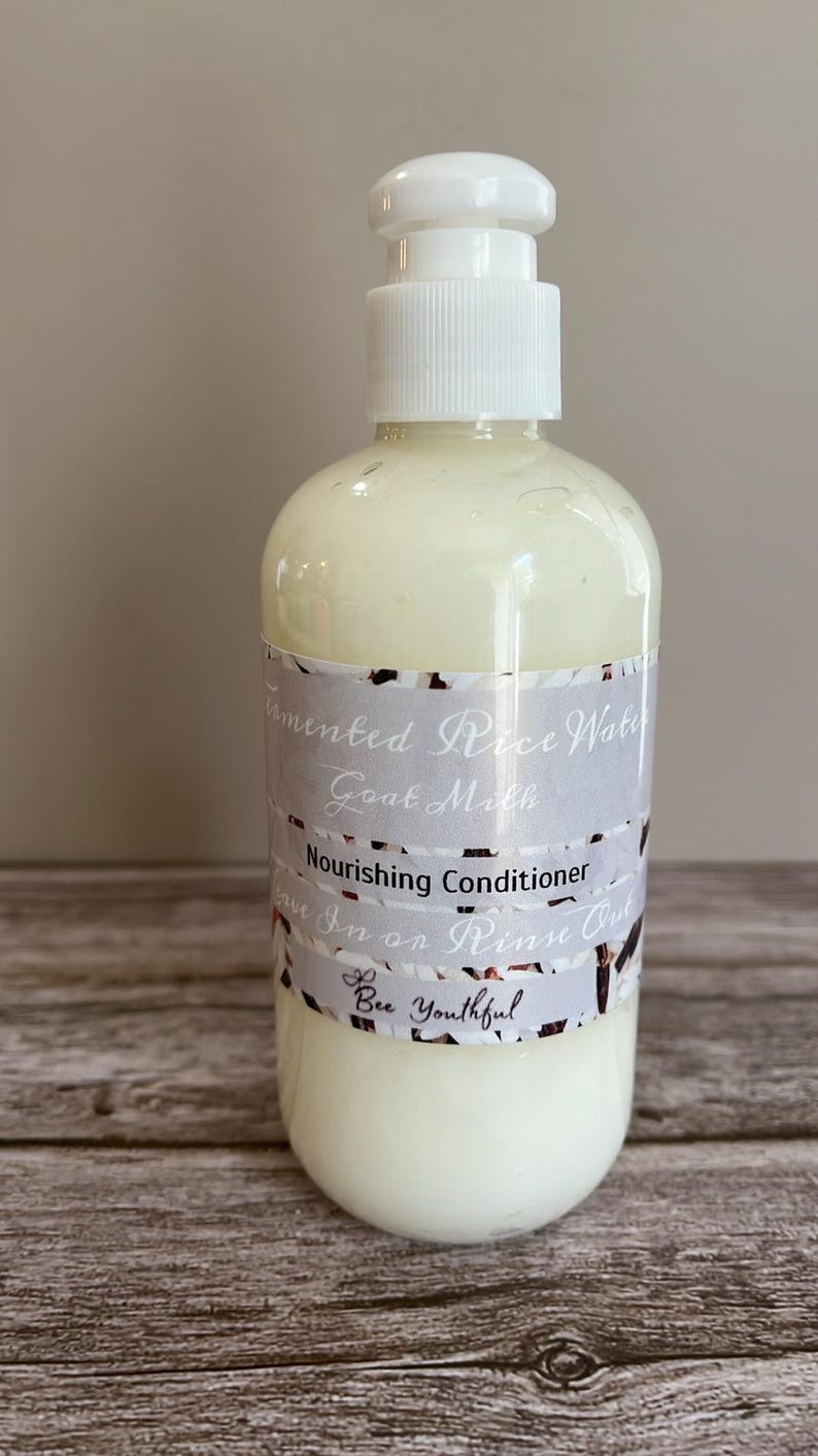 Puede incluir: Una botella de pl&aacute;stico blanco con dispensador de bomba, llena de un l&iacute;quido cremoso blanquecino. La etiqueta dice "Fermented Rice Water Goat Milk Nourishing Conditioner". El producto es de "Bee Youthful".