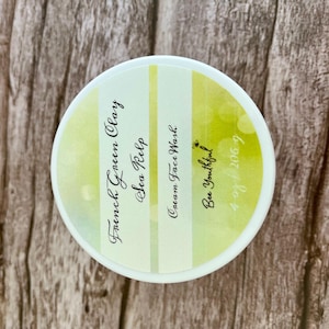 May include: A white jar with a yellow and green striped label. The label reads "French Green Clay Sea Kelp Cream Face Wash Bee Youthful 4/28/2067".