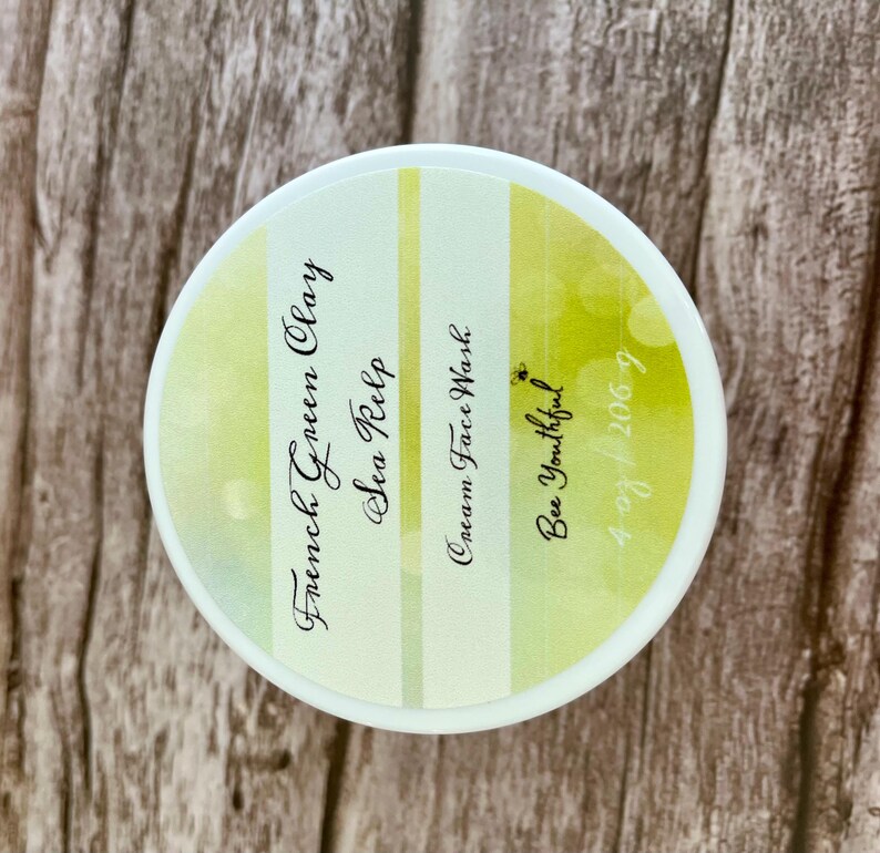May include: A white jar with a yellow and green striped label. The label reads "French Green Clay Sea Kelp Cream Face Wash Bee Youthful 4/28/2067".