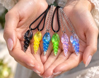 May include: A collection of six spiral-shaped glass pendants in black, yellow, blue, green, pink, and iridescent blue. Each pendant hangs from either a black cord or a silver-toned metal chain, featuring a translucent, twisted shell design.