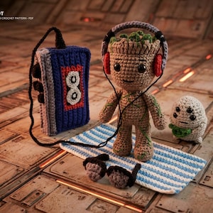 May include: A crochet amigurumi figure of a tree-like character wearing purple and red headphones, accompanied by a blue cassette player, a small white creature, and dark sunglasses on a blue and white striped mat. Text reads GROOT AMIGURUMI CROCHET PATTERN - PDF.