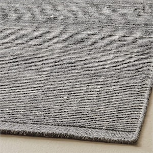 May include: A rectangular area rug featuring a dark charcoal gray color with a prominent horizontal ribbed texture. The surface displays a woven pattern with subtle variations in tone, including small flecks of lighter gray and white fibers.