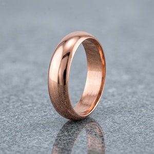 May include: A polished rose gold ring with a smooth, rounded exterior surface and a high-shine metallic finish. The band features a simple, solid construction with a consistent width throughout, reflecting light across its curved, reflective surface.