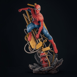 May include: A detailed Spider-Man action figure in a red and blue suit, posed dynamically on a yellow construction crane structure. The base features a red fire hydrant and dark, textured rubble, creating a scene of urban action and movement.