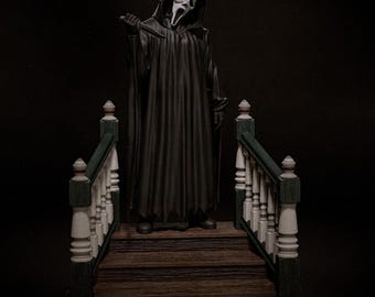 Puede incluir: Una figura de un personaje encapuchado con una máscara de fantasma blanca y una túnica negra larga, sosteniendo un cuchillo pequeño. La figura se encuentra sobre una escalera de madera marrón con barandillas blancas y verde oscuro a los lados.