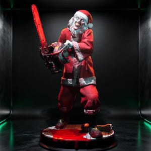 May include: A figurine of a sinister Santa Claus wearing a red and white suit, holding a bright red chainsaw. The character has a pale face, wild white hair, and a menacing grin. The base features a pool of red liquid and a severed limb.