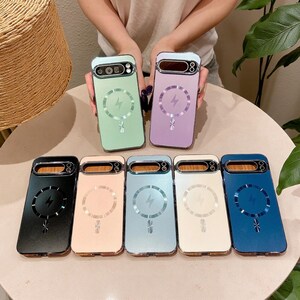 May include: A collection of seven smartphone cases in various colors including light green, lavender, black, peach, light blue, cream, and dark blue. Each case features a metallic camera cutout and a circular magnetic charging ring design.