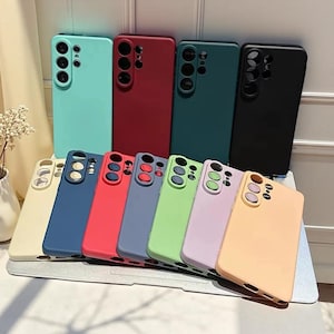 Könnte beinhalten: Eine Sammlung von elf Smartphone-Hüllen in verschiedenen Unifarben, darunter Minzgrün, Dunkelrot, Dunkelgrün, Schwarz, Creme, Marineblau, Hellrot, Schieferblau, Limettengrün, Lavendel und Pfirsich, jeweils mit einem erhöhten Kameraausschnitt.