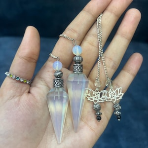 Peut inclure: Deux pendules en cristal opaline facetté avec des capuchons en métal argenté et de petites perles d'opaline rondes fixées à des chaînes argentées. Les chaînes comportent des breloques fleur de lotus argentées et de petites perles noires.