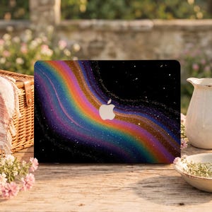 May include: A laptop skin featuring a vibrant, swirling rainbow nebula design against a deep black background filled with tiny white stars. The iconic silver Apple logo is centered on the lid, contrasting with the colorful cosmic pattern.