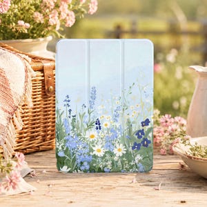 Può includere: Una custodia rettangolare per tablet con sfondo azzurro e un'illustrazione stampata di un campo di fiori selvatici, tra cui margherite bianche, piccoli fiori blu e steli verdi, con un design a tre ante e linee di piegatura verticali.