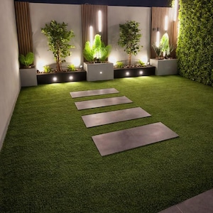 Könnte beinhalten: Ein Gartenbereich mit einer grünen Kunstrasenfläche und vier rechteckigen grauen Steinplatten, die zu einer Wand führen. Die Wand ist mit vertikalen Holzlatten, integrierter Beleuchtung und grauen Pflanzkübeln mit grünen Sträuchern versehen.
