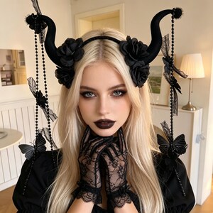 May include: A black headband featuring two curved horns, decorated with black fabric roses, dangling beaded chains, and black butterfly accents. The accessory is paired with sheer black lace gloves that feature intricate floral patterns.