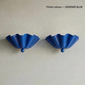 May include: Two dodger blue wall sconces with a scalloped, ruffled edge design. Each fixture features a central spherical accent at the base. The text Finish colour--- DODGER BLUE is visible in the upper right corner of the image.