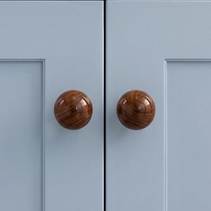May include: Two spherical cabinet knobs made of polished dark brown wood with a visible natural grain pattern. The knobs are mounted on a light blue cabinet door with a recessed panel design, featuring a smooth finish and a glossy surface texture.