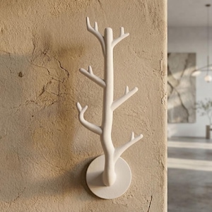 May include: A matte white wall-mounted coat rack shaped like a stylized tree branch. The structure features a central vertical post with six protruding hooks extending outward at various heights, all anchored to a circular base plate.
