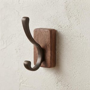 May include: A wall-mounted hook featuring a dark brown, curved metal hook attached to a rectangular, natural-toned wooden base. The metal hook has a smooth, matte finish with a double-pronged design, while the wooden mount displays a visible grain.