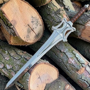 May include: A double-edged steel sword featuring a pointed blade, a symmetrical silver-toned crossguard with intricate cutouts, and a brown leather-wrapped handle topped with a metallic pommel, showcasing a polished finish and sharp edges.