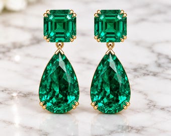 May include: A pair of drop earrings featuring a square-cut green gemstone at the top and a larger pear-shaped green gemstone suspended below. Both stones are set in gold-toned metal prongs, creating a symmetrical design with vibrant green hues.