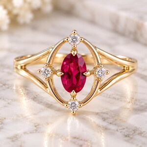 Könnte beinhalten: Ein Goldring mit einem zentralen, oval geschliffenen, leuchtend roten Edelstein in einer elliptischen Fassung. Vier kleine, runde, klare weiße Akzentsteine sind an den vier Punkten der Fassung angebracht, die mit einer geteilten Ringschiene verbunden ist.