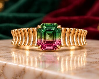 May include: A gold ring featuring a rectangular emerald-cut bicolor gemstone that transitions from green at the top to pink at the bottom. The band is crafted with a series of vertical, curved, ribbed gold segments surrounding the center stone.
