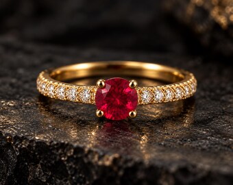Peut inclure: Une bague en or ornée d'une pierre précieuse ronde d'un rouge éclatant au centre, maintenue par quatre griffes. L'anneau est agrémenté d'une série de petites pierres claires taillées en rond incrustées sur les côtés, créant un effet scintillant.